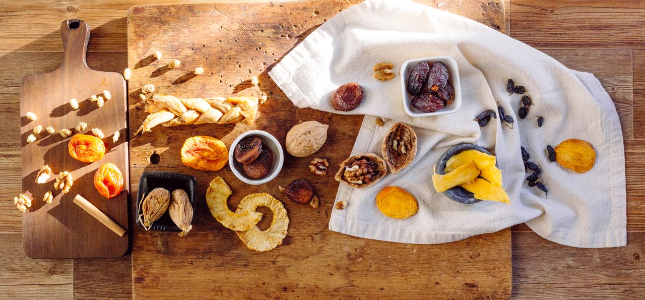 A variety of dried fruits displayed on a wooden table with cloth and cutting board.